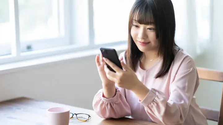 自宅でスマートフォンから予約メッセージを送る女性
